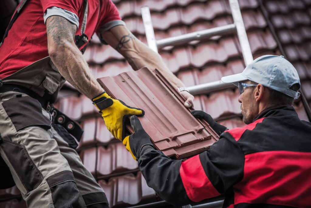 Roofers installing red roof tiles for accurate roofing cost estimation.