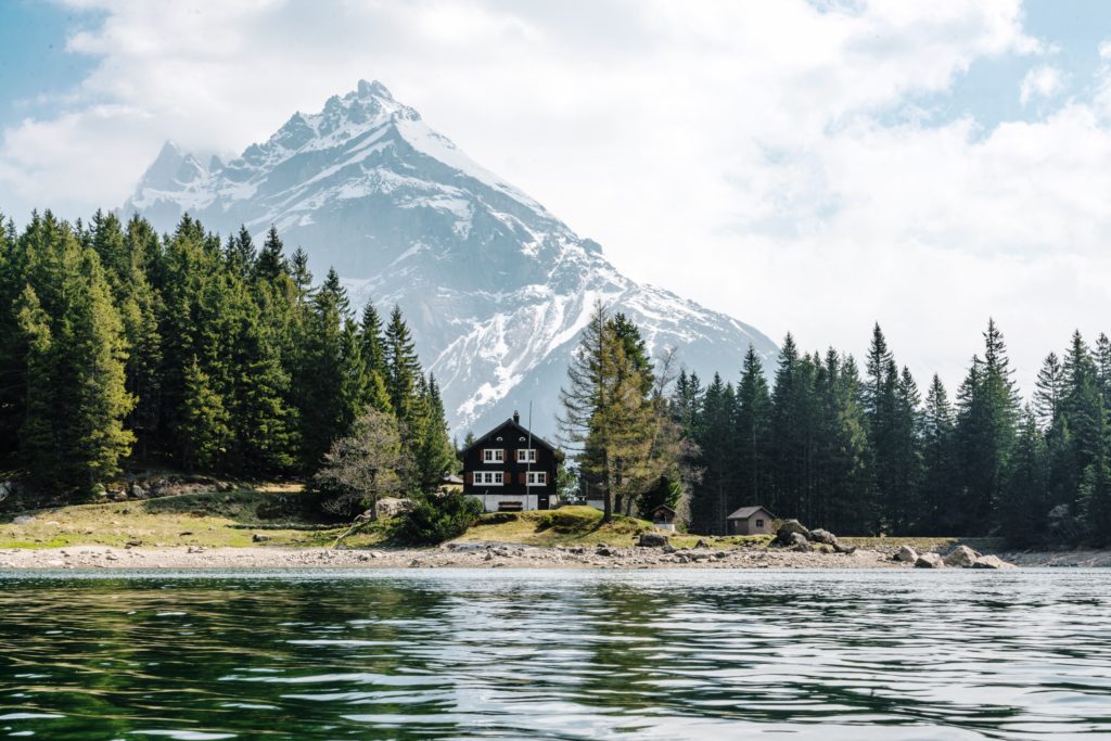 a house by a lake with trees and mountains in the background