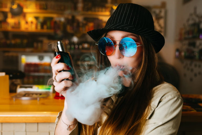 Vaping girl. Young hipster woman vape e-cig at the vapeshop. Hip-hop style. Closeup