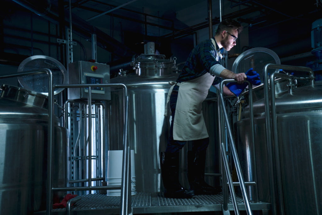 Side view of young man in brewery looking into fermentation tank