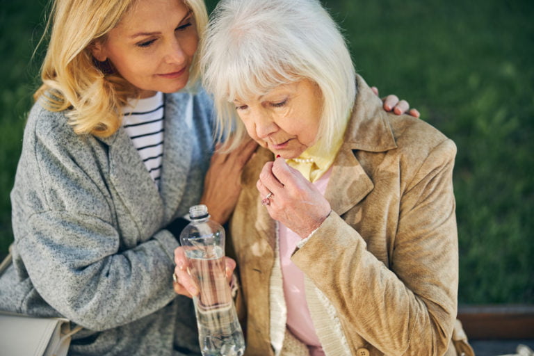 Elderly woman drinking water while another female sitting near her