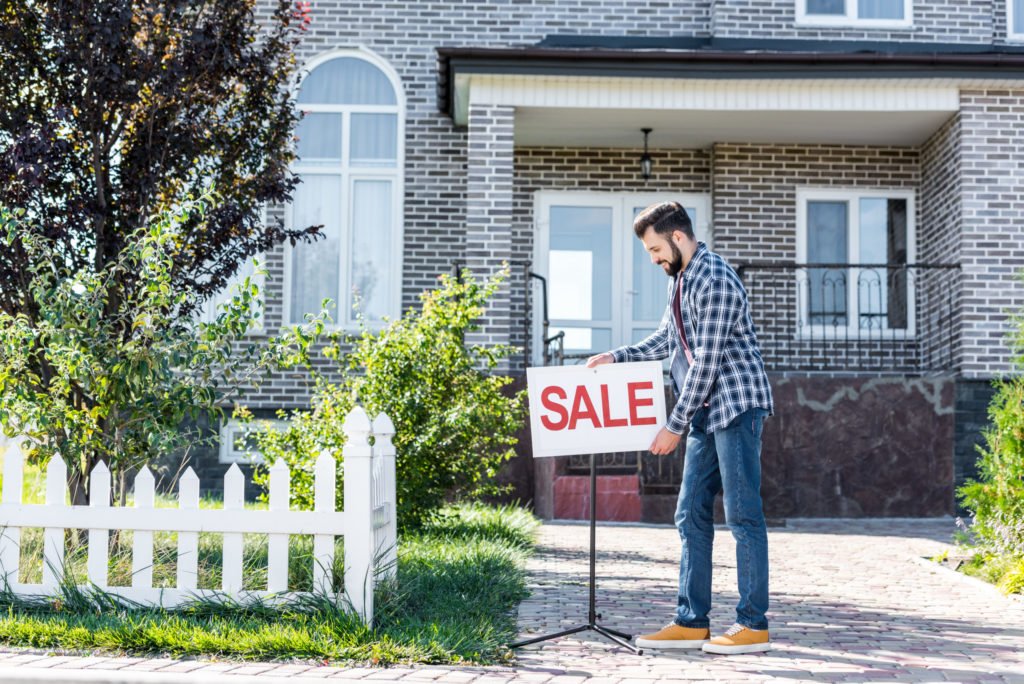 home, young man with sale board selling his new house utc scaled