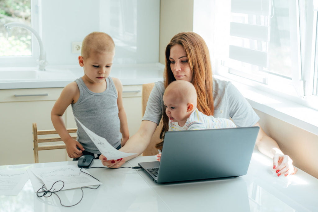 Business woman babysitting children and working online on a laptop.