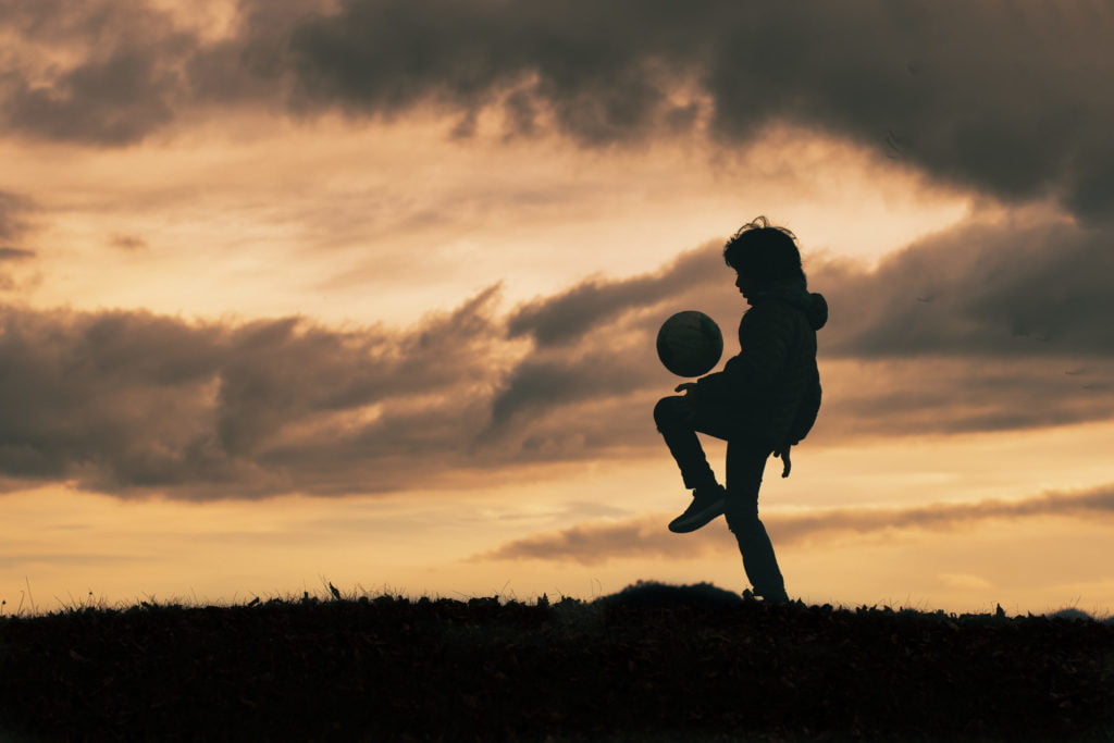 Child in silhouette dribbles and plays with soccer