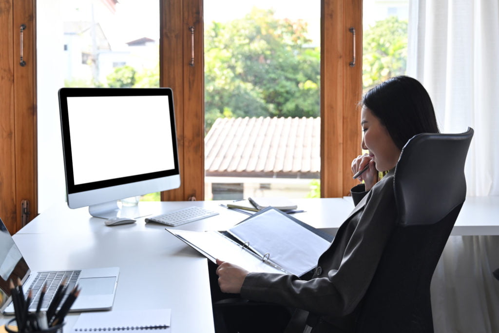 Rear view of businesswoman working on computer and checking financial document.